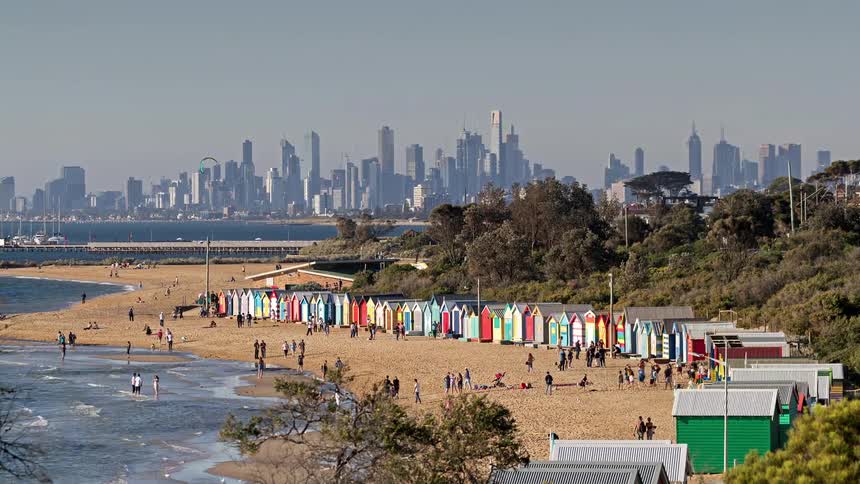 Colorful huts lined on sand with skyscrapers in background