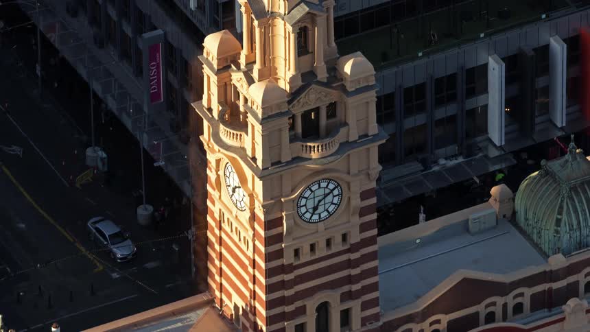 Sunlight shines on a clock tower as pedestrians and automobiles move on the city streets