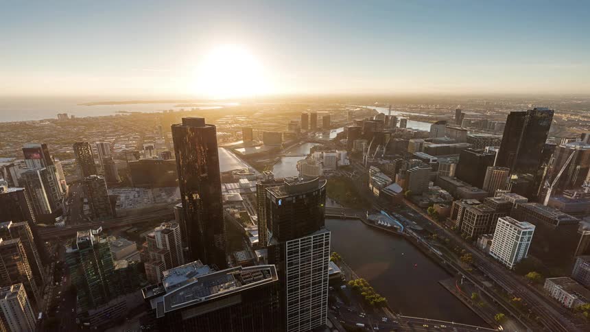 A high angle timelapse shows the sun setting over a city and reflects the changing sky while shadows stretch across skyscrapers and the urban grid transitions from bright daylight to a glowing night