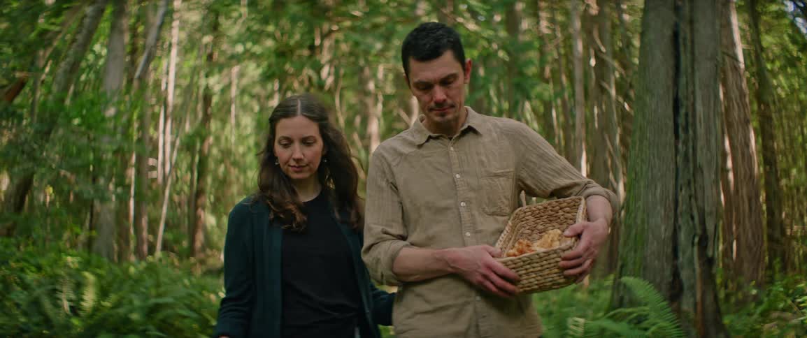 Couple walking quietly through a forest while carrying a basket of freshly foraged mushrooms