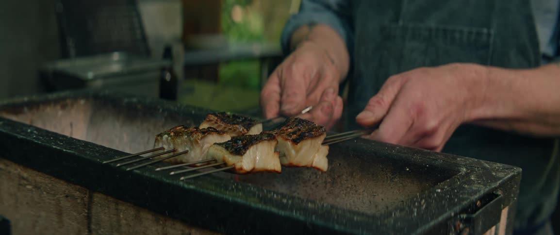 The man flips the skewers with meat on the barbecue