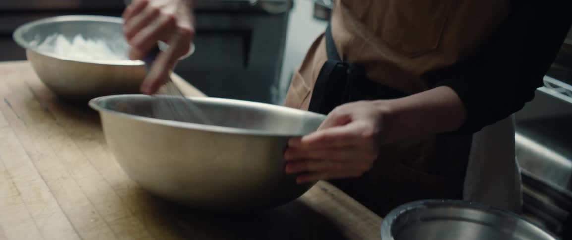 Hands mix thick batter in a metal bowl on a kitchen counter