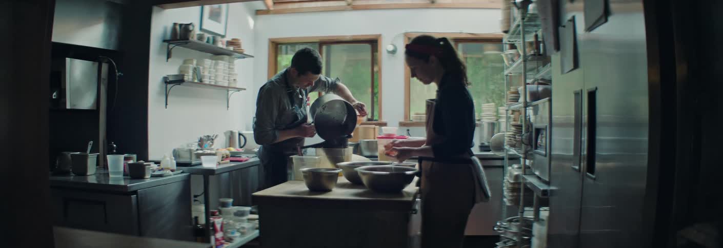 Two cooks prepare ingredients in a professional kitchen with bowls and utensils on the counter
