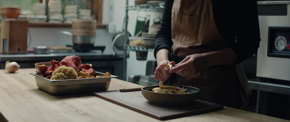 Person prepares vegetables on wooden counter beside tray of fresh mushrooms