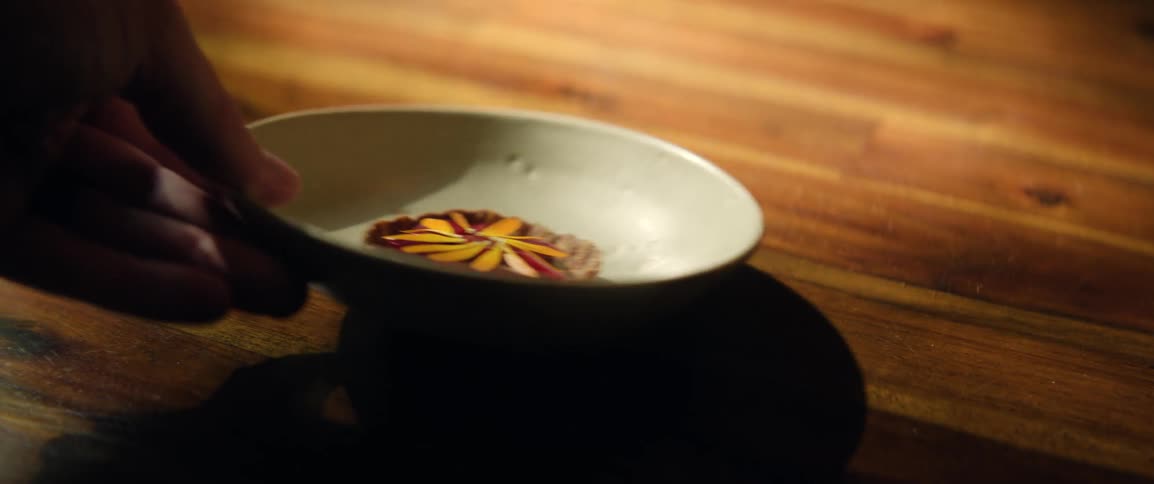 Human male hand picking up a dish with a small pie from a wooden table during day time