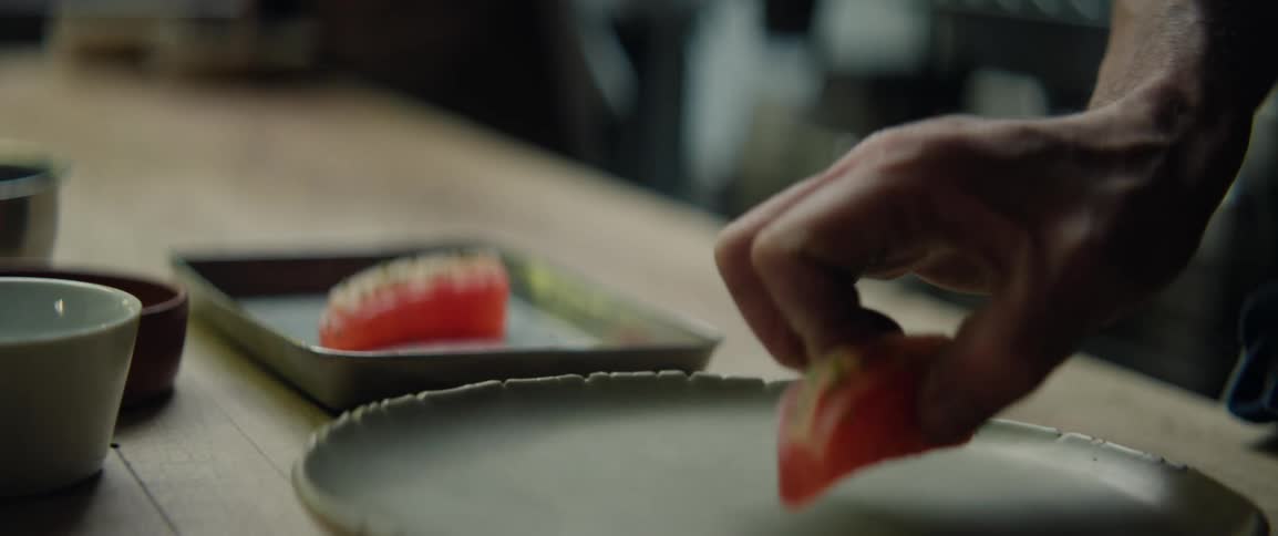Human male hand assembling a piece of sushi on a dish over a wooden table indoors