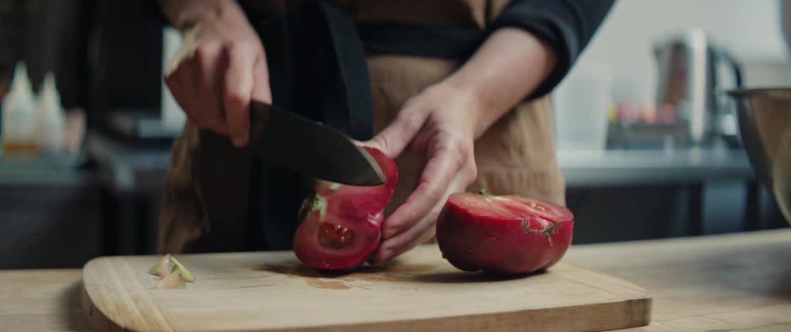 Tomato being sliced on wooden board during food preparation