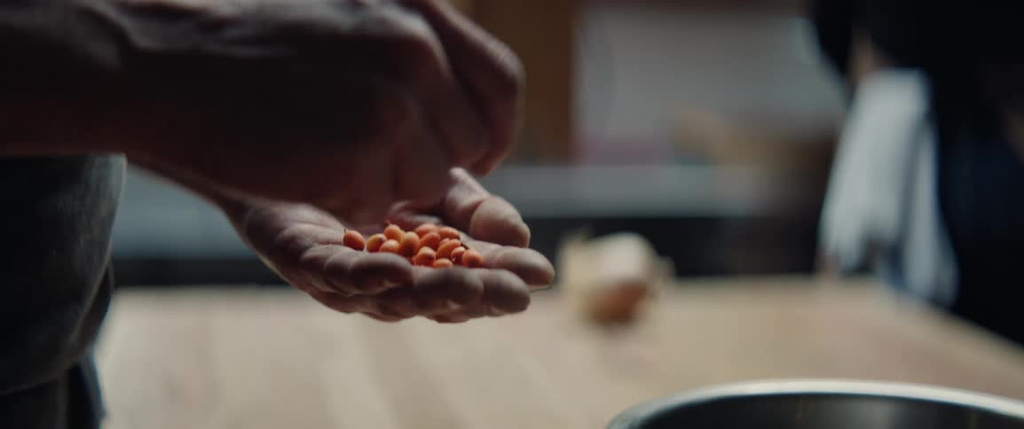 Adult male hands picking beans and putting them on a bowl over a wooden table indoors