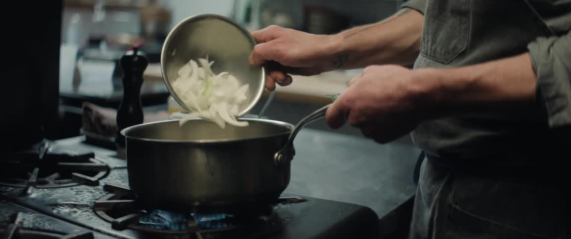 Sliced onion being poured into pot over blue flame