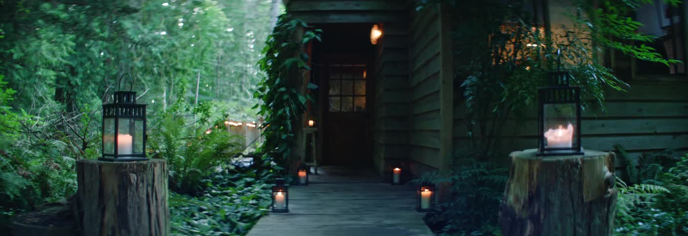 Wooden cabin surrounded by greenery and lit lanterns