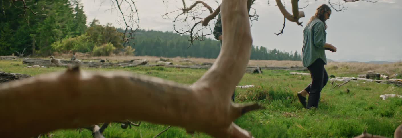 Two individuals kneeling on grassy field with branches and basket