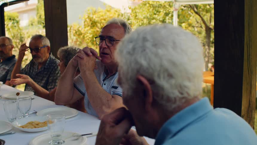 Group of adults gathered at outdoor table under wooden structure