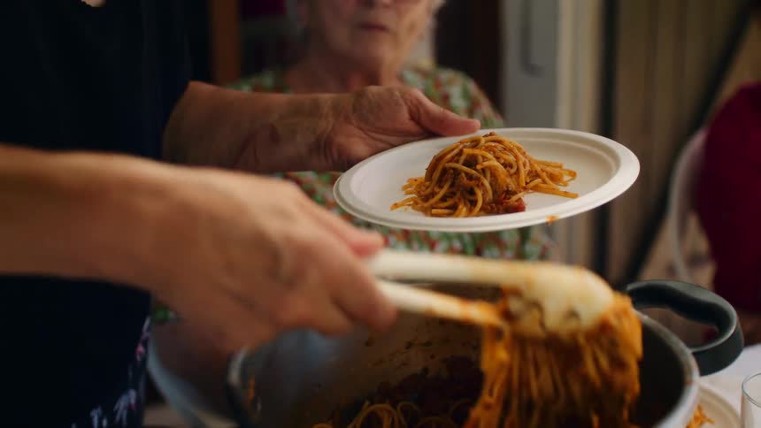Spaghetti with sauce being served onto plate during a warm meal gathering