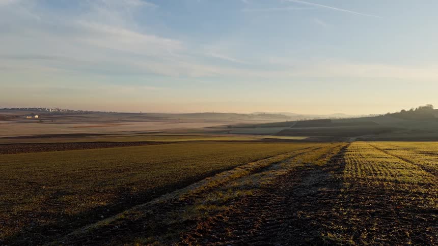 Golden morning sunlight illuminates vast rolling farmland as the camera pans across the countryside