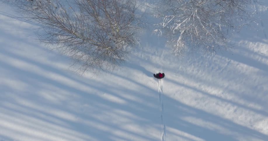 A person in red treks through deep snow leaving a trail across the winter landscape