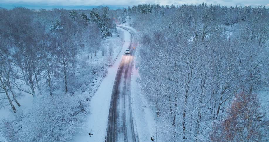 A dark asphaltcolored ribbon that cuts vertically through the center of the frame it curves gently toward the top left showing visible tire tracks where the snow has been cleared or melted creating a sharp contrast against the surrounding white