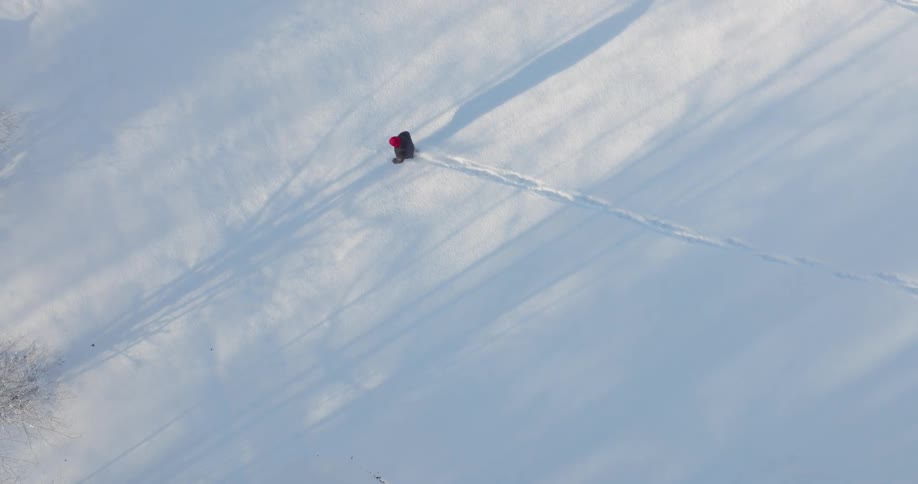 A man casts a shadow as he walks across a snowy field
