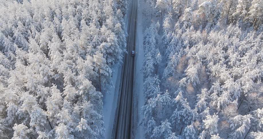 A vehicle moves down an empty highway that cuts through a snowy forest