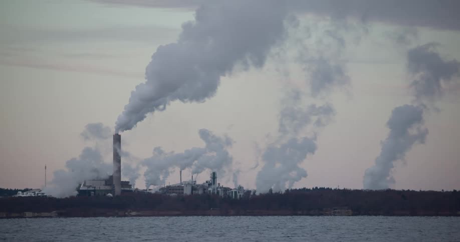 Factory with chimneys releasing pollutants by the sea