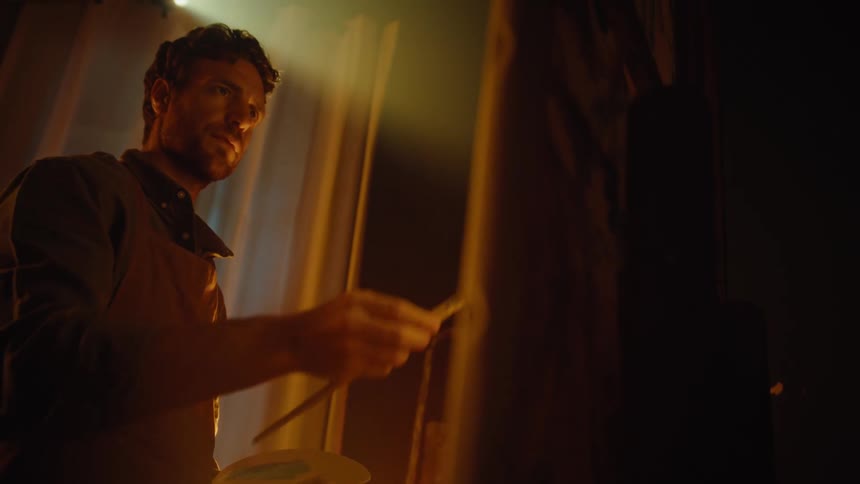 Man applies paint with a brush onto a vertical surface under warm indoor lighting
