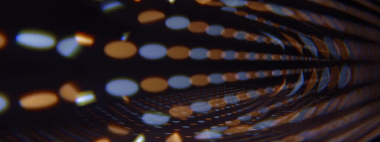 This video features a rhythmic pattern of glowing orange and blue circular lights arranged in a curved tunnellike perspective the softfocus bokeh effect creates a sense of motion and depth giving the abstract visual a futuristic or cinematic feel