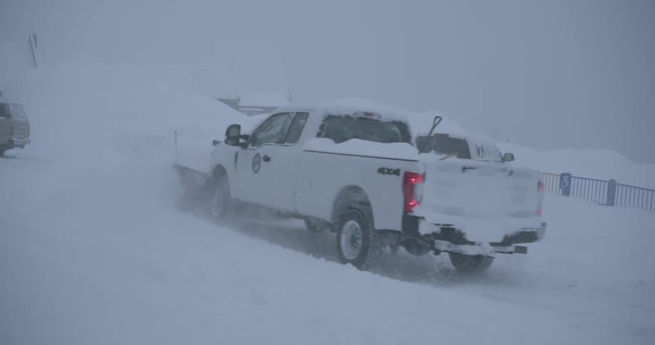 Government vehicle with a snowplow attachment clears the streets of a snow covered town on a winter day