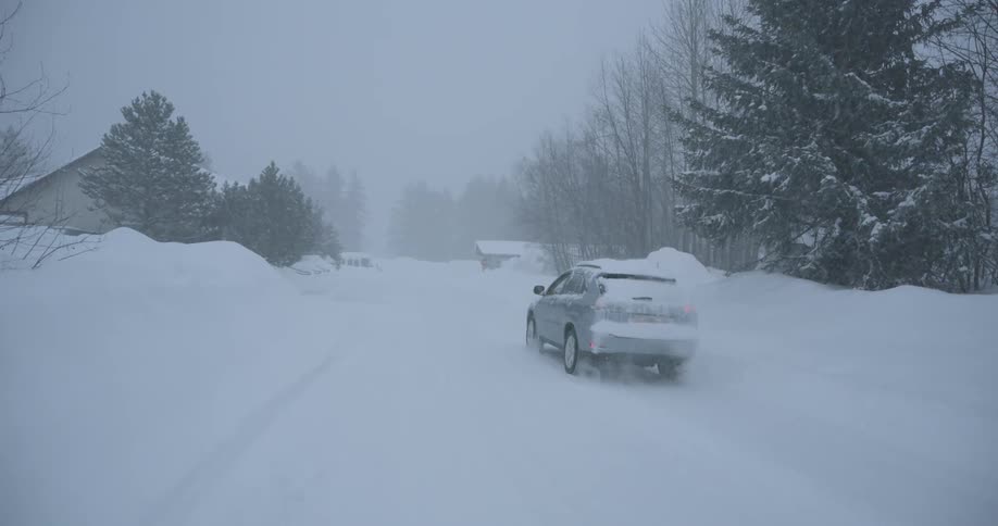 Car drives along a snowcovered road during a heavy snowstorm with trees around