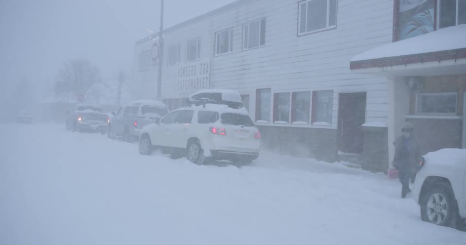 During a heavy blizzard cars are parked along a snowcovered street in front of a supermarket as a person braves the storm to walk toward the entrance