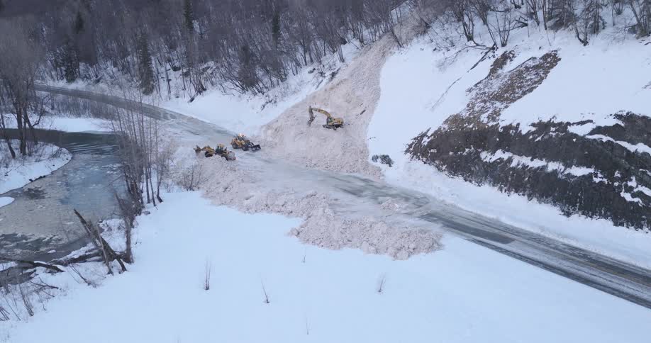 Tractors are working to clear snow from the highway that was caused by an avalanche