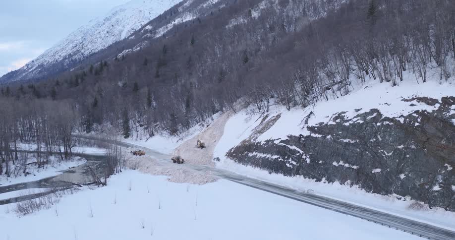 Three snowplow tractors are clearing an avalanche from a remote mountain road