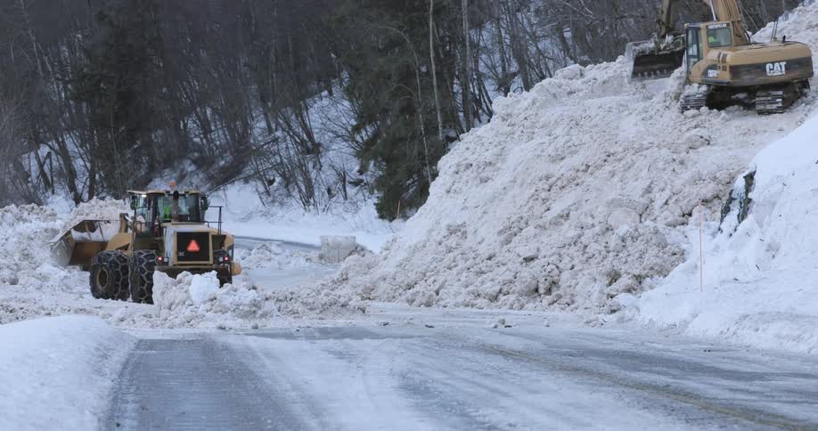 Tractors are moving large amounts of snow from a roadway