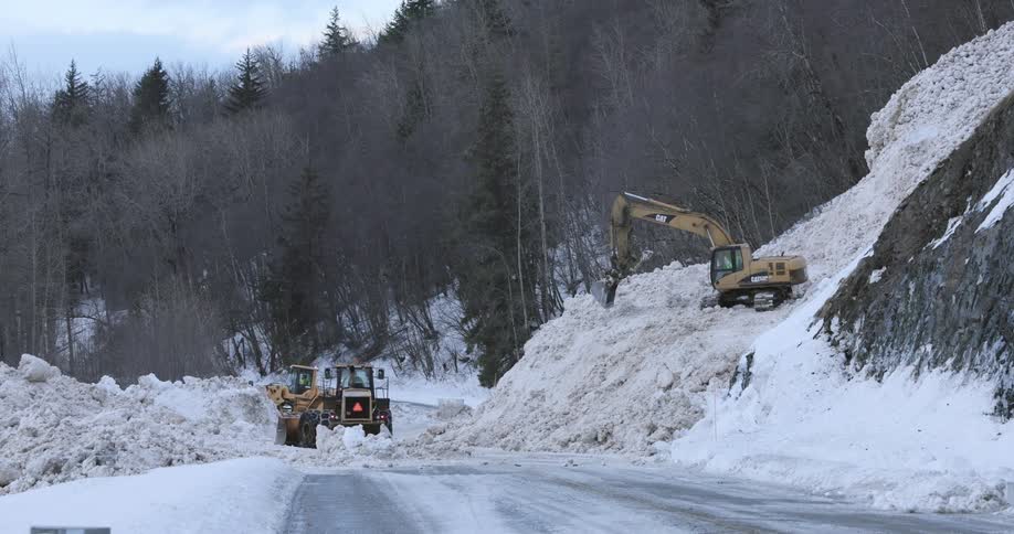 Three snowplow tractors clear deep snow off a mountain road