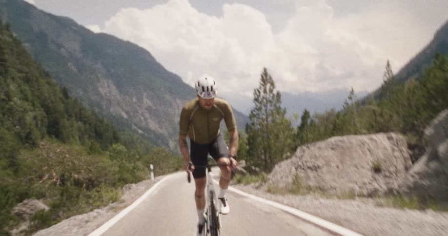 Cyclist climbs a paved mountain road between rocks and alpine vegetation