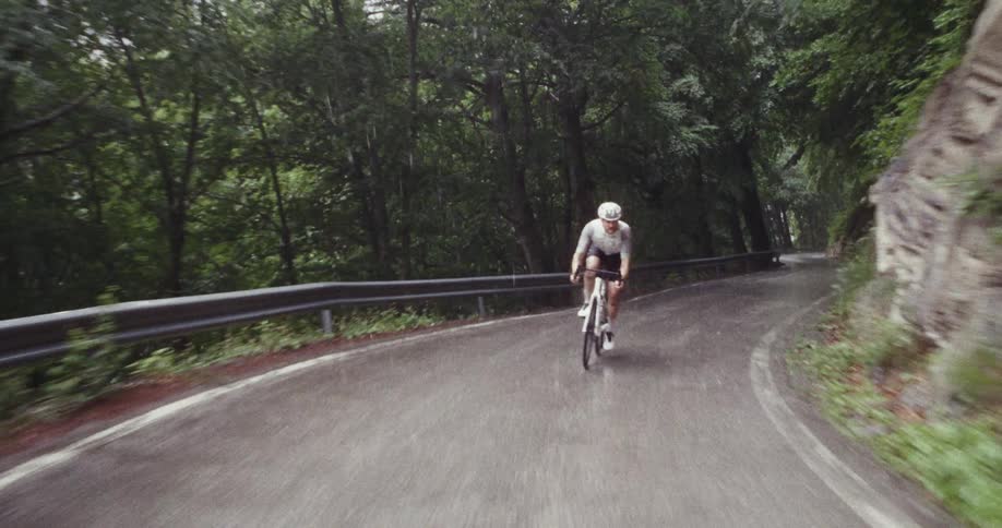 Man rides his bicycle on a forested mountain road in the rain