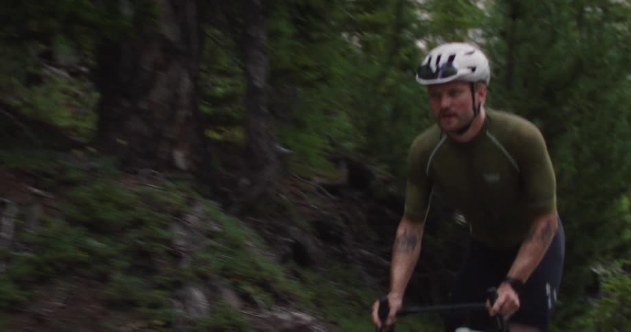 A determined cyclist in a green jersey and white helmet rides along a lush forested road