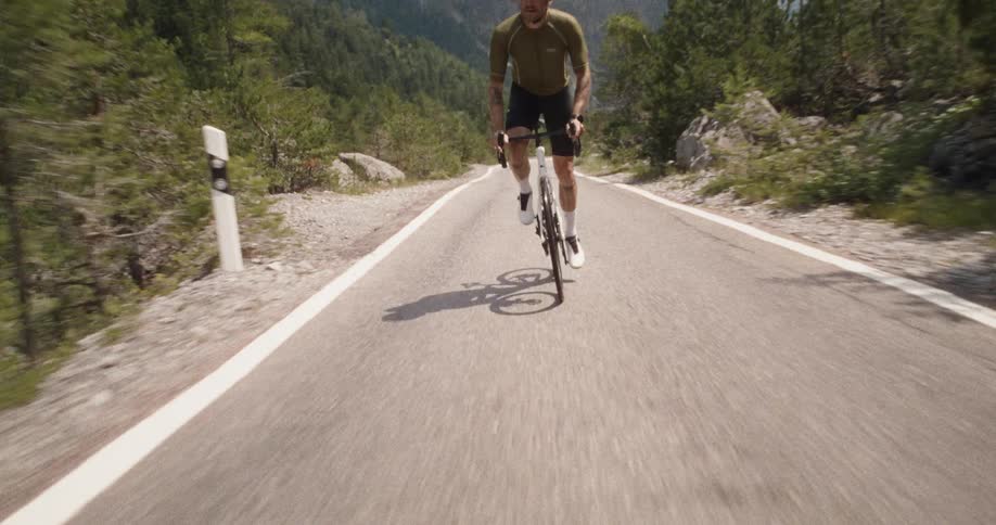 Lone male cyclist pedals along a paved path through forested mountainous terrain on a foggy and cloudy day