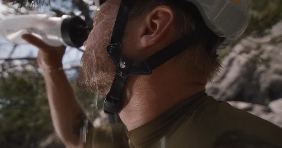 A man in a helmet splashes water from a bottle over his face to cool down