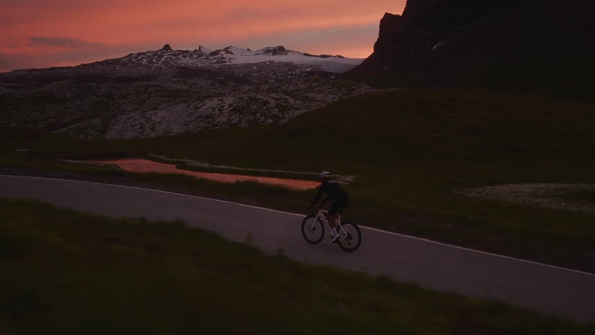 Man riding his bicycle on a mountain road under a red sunset sky