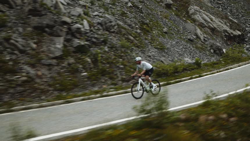 Cyclist rides at high speed along a winding road in a rocky mountainous area