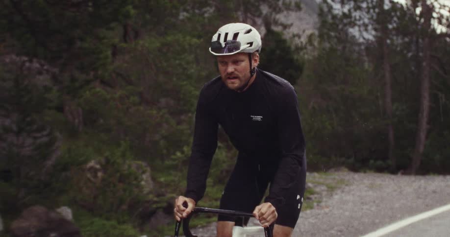 A view shows a person wearing a helmet and a black long sleeve shirt as they mount a white bicycle on a rocky mountain during the day