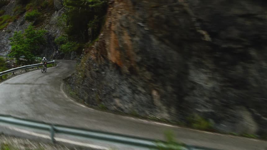 Cyclist rides along a narrow road beside a rocky cliff with a metal guardrail