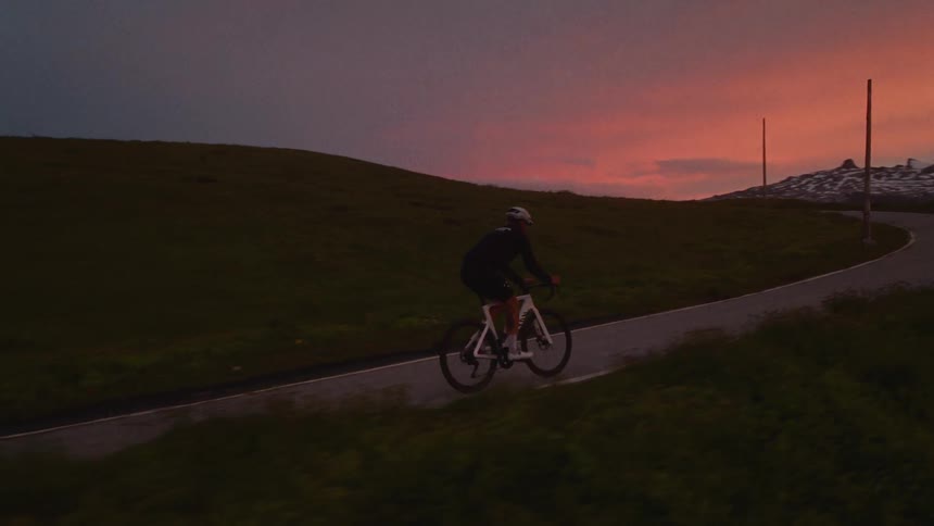 Cyclist rides along a rural road at dusk with an orange sky on the horizon