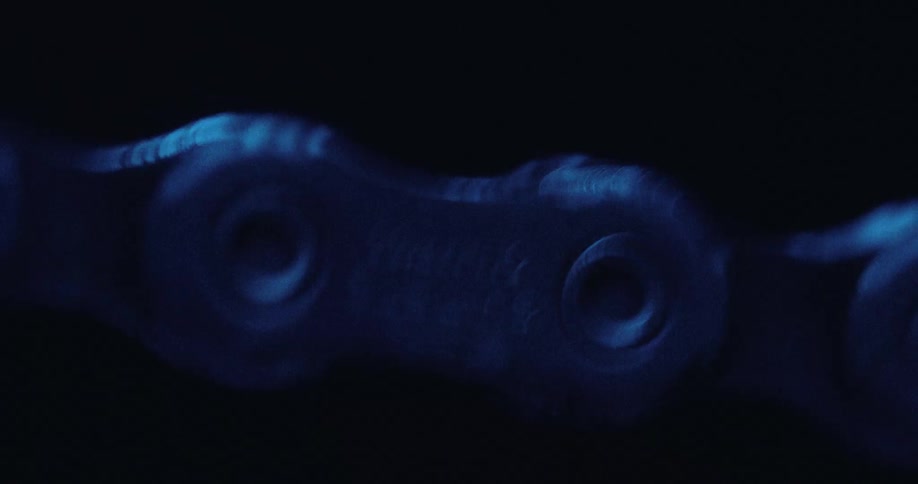 Bicycle chain in closeup under blue lighting with links in continuous motion