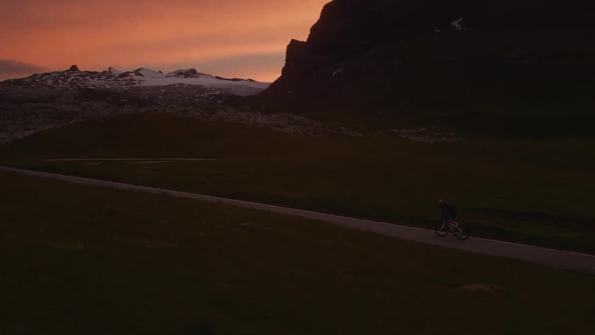 Man riding his bicycle on a mountain road under a red sunset sky