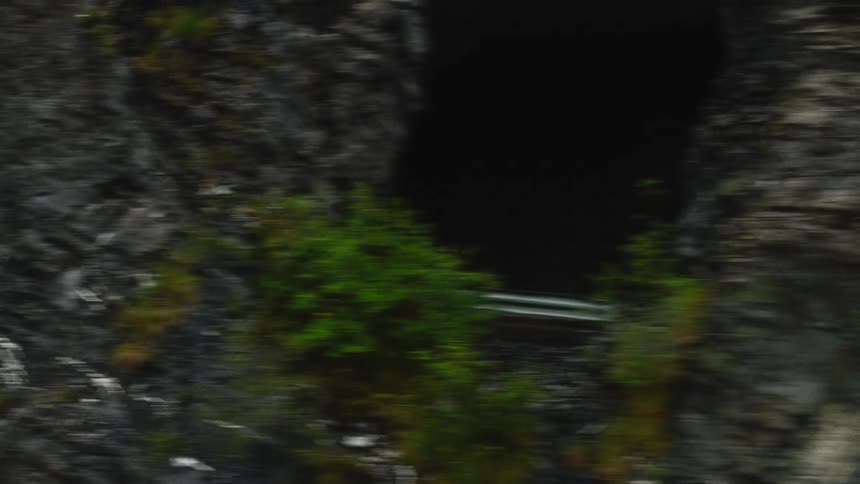 Cyclist rides at a fast pace along a narrow road with a guardrail beside a rocky cliff