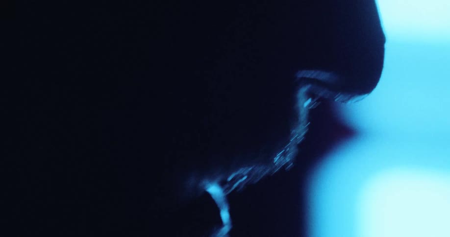 Bearded facial profile lit by blue light outlining contours against a dark background