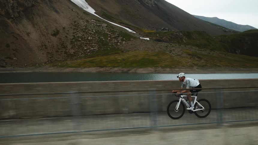 Cyclist rides along an elevated roadway with a concrete barrier in an arid mountainous landscape