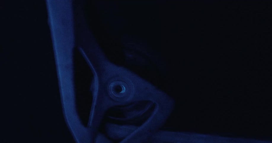 A close up view shows a part of a bicycle as it moves in a dark area with blue light