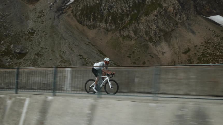 The man rides his bike over the dam by the mountain