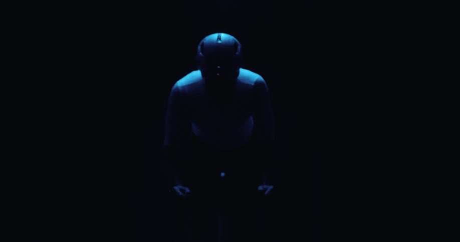 Human figure centered under blue lighting in a dark environment with head tilted downward